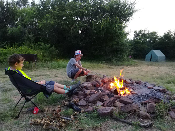 Scouts sitting beside a campfire, with a tent in the background.