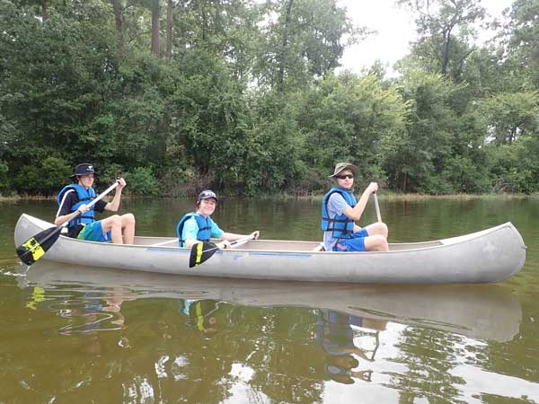 Three Scouts wearing life jackets and paddling a canoe.