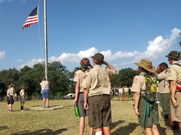 Scouts saluting as an American flag is raised at camp.